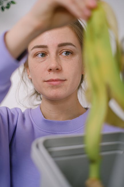 A person’s hand is seen holding a white paper bag, emptying kitchen vegetable peelings and food scraps into a round white compost bin placed on a bright green plastic tray, which sits on a tiled sur