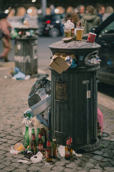The image displays a close-up view of several crushed and partially flattened aluminium cans, with metallic silver surfaces reflecting light. The cans are stacked haphazardly, with some overlapping ea