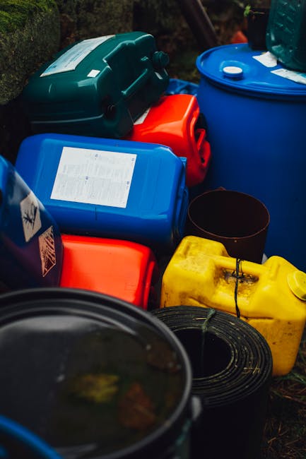 A large outdoor pile of mixed household waste and rubbish situated on a patch of bare earth and sparse grass, including broken electronic appliances such as a washing machine and miscellaneous metal a